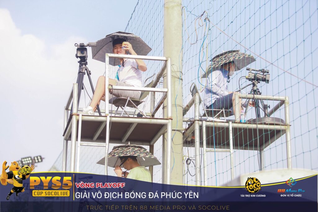 Camera man làm việc dưới cái nắng gắt với nụ cười tươi trên sân